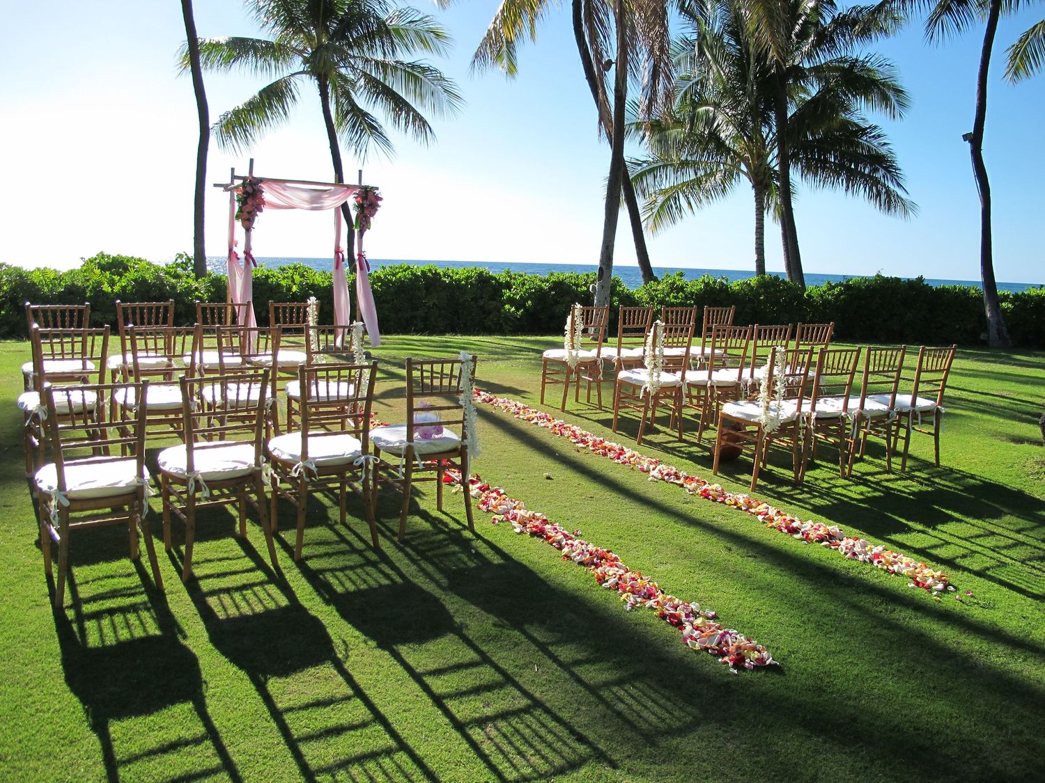 Tropical outdoor wedding ceremony setup with gold chiavari chairs, floral aisle, and ocean view backdrop.