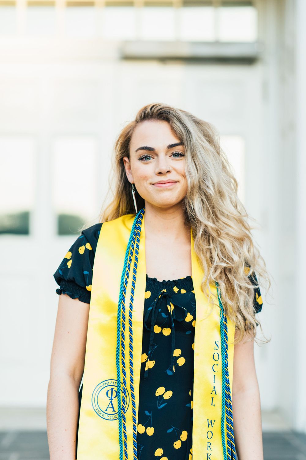 A masters graduate posing in her cords and stole for the camera with curly hair in front of an academic building