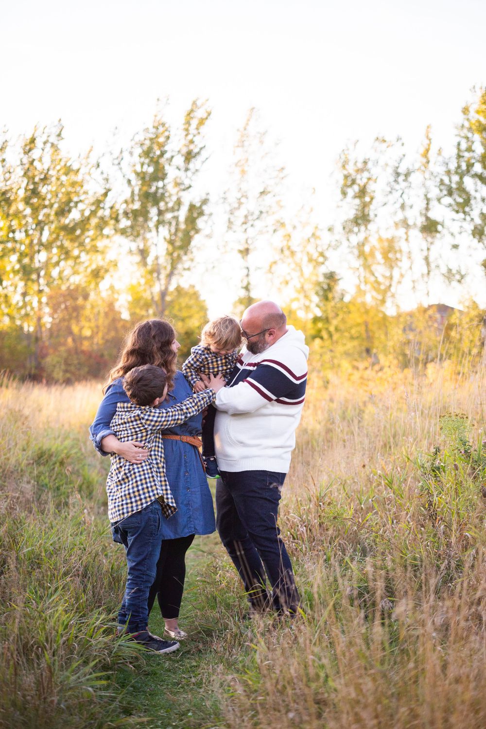 A family of four shares a warm embrace in a golden sunlit meadow during fall.