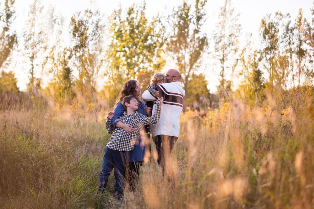 A happy family hugs together in a field of tall golden grass at sunset.