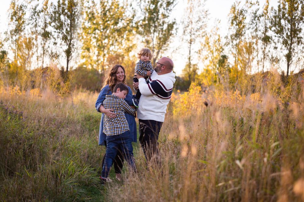 A family of four walks and plays in a sunlit autumn meadow with tall grass.