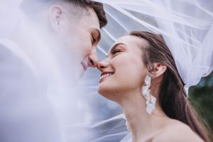 Bride and groom smiling intimately under wedding veil in close romantic portrait.
