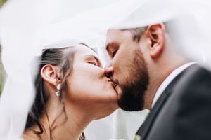 Bride and groom share an intimate kiss under a flowing white veil at their wedding celebration.