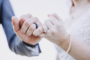 Close-up of newlyweds holding hands showing wedding rings and pearl bracelet on wedding day.