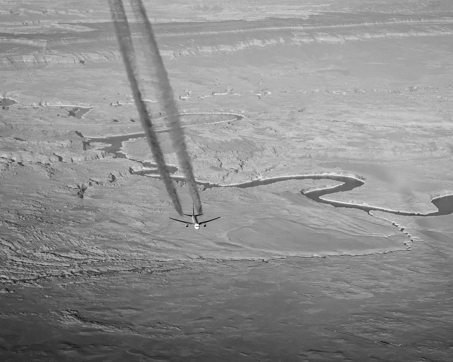 Aerial black and white photograph of shadows cast by plane over winding river landscape.