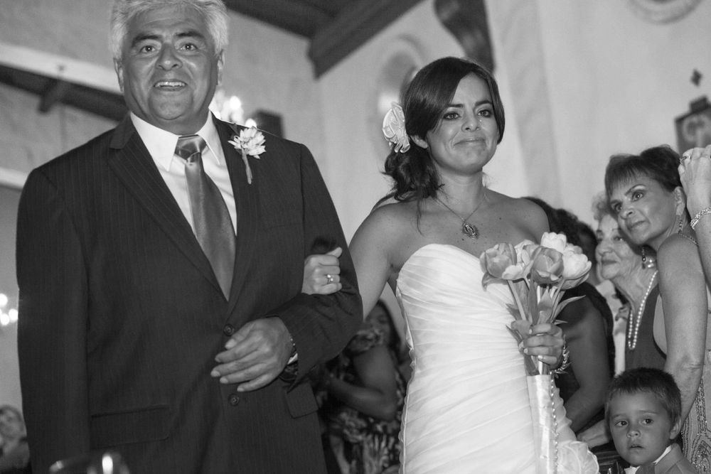 Black and white wedding photo showing a bride in a strapless gown walking arm in arm with an older gentleman.