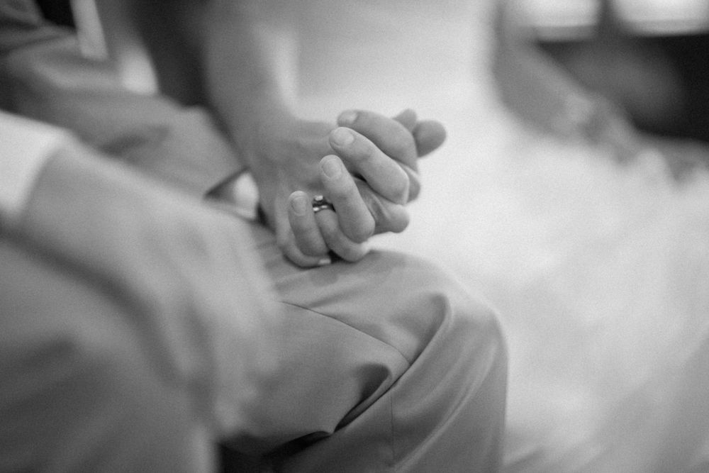 Black and white image showing two hands clasped together intimately with a ring visible.