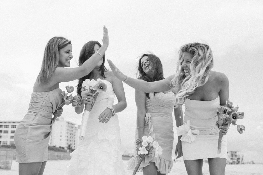 A joyous black and white photo of bridesmaids celebrating in strapless dresses while holding bouquets outdoors.