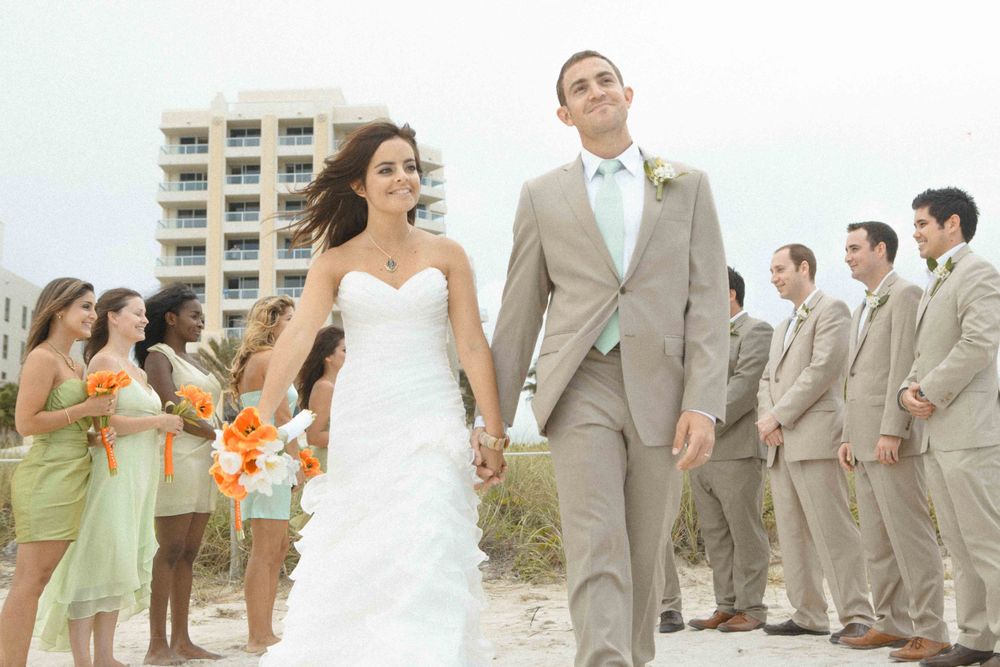 A seaside wedding features a procession with bridesmaids in mint green dresses and groomsmen in khaki suits on a beach.