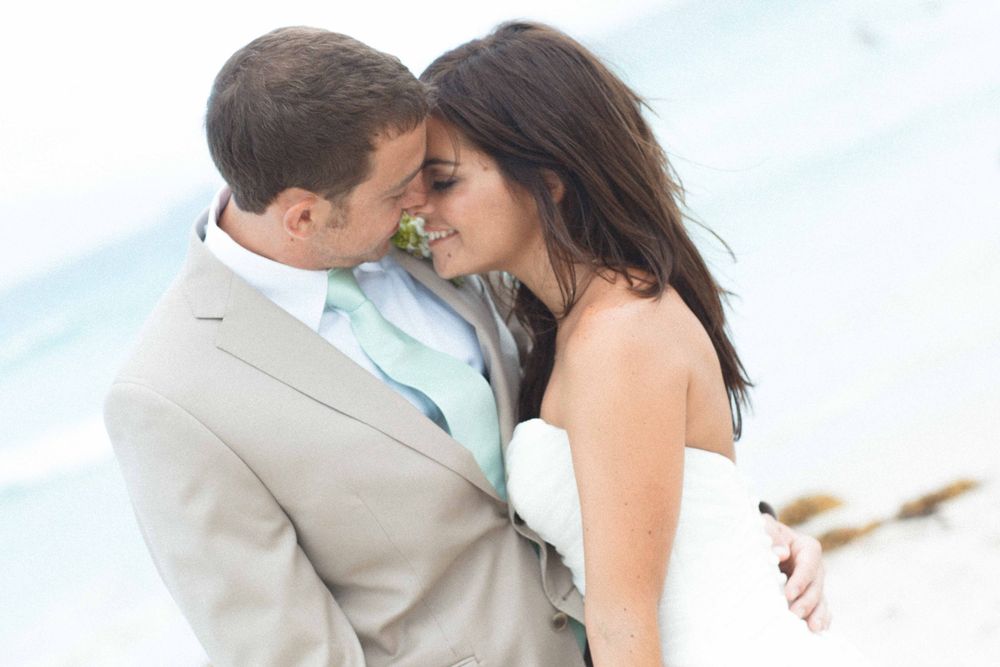 A couple in wedding attire shares an intimate moment while posing outdoors near a body of water.