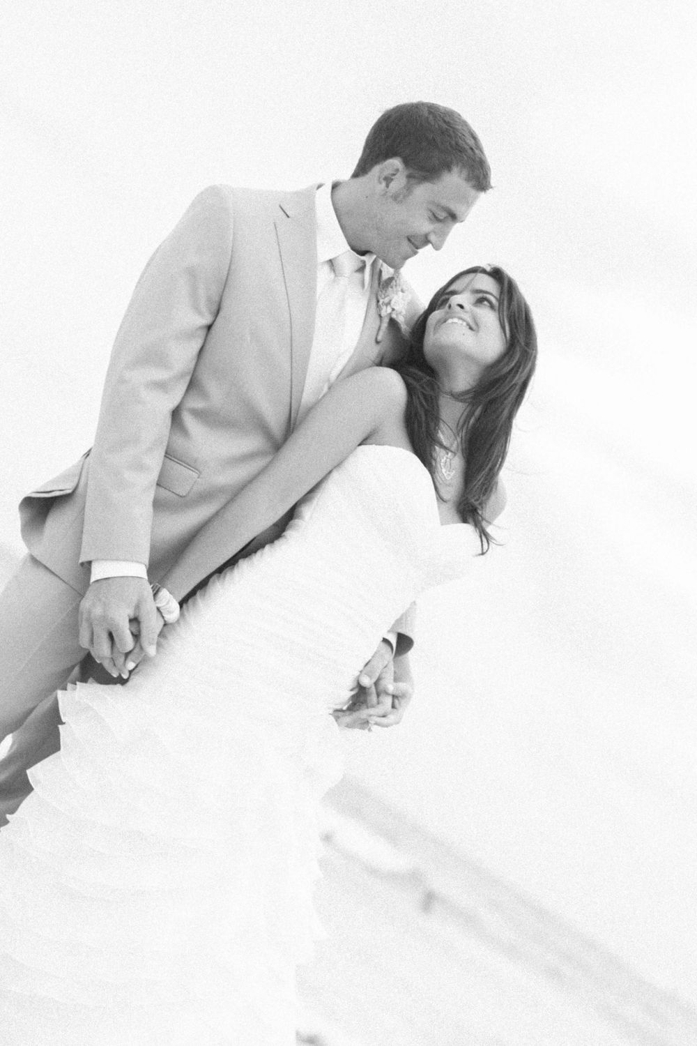 A romantic black and white wedding photo of a couple in formal attire embracing against a light background.