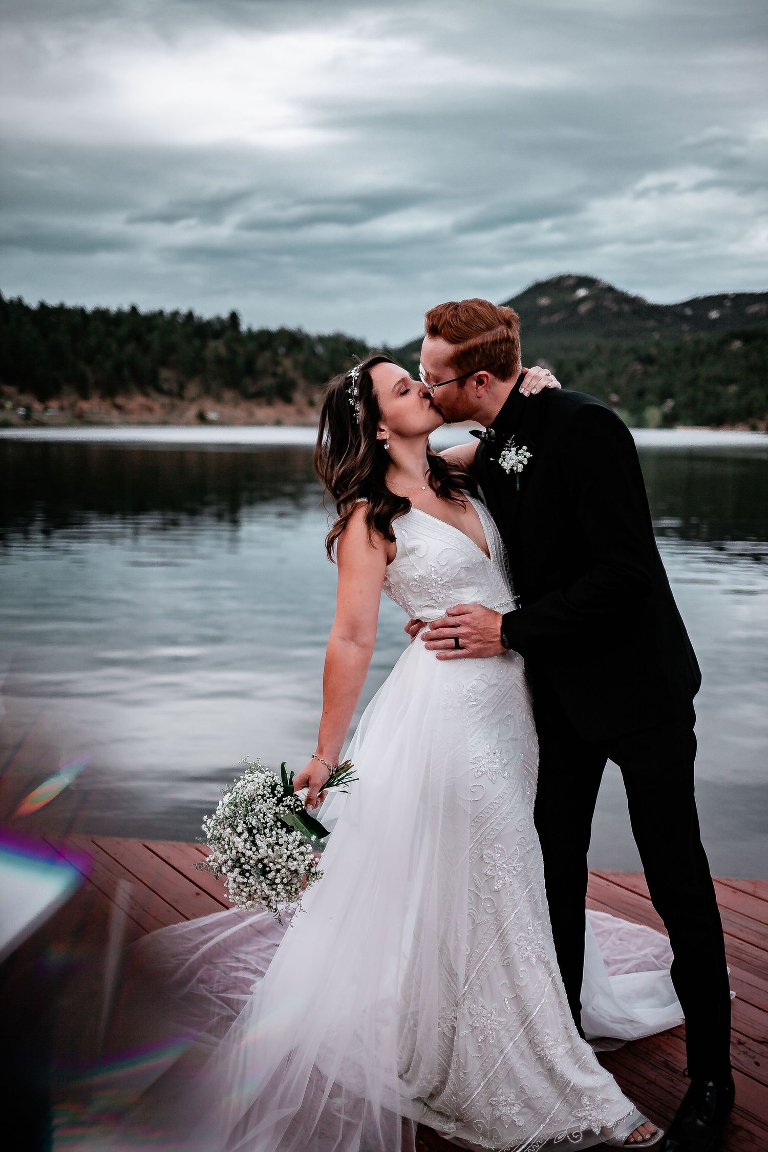 Newlyweds sharing romantic kiss on dock with mountain lake backdrop. Denver wedding Photography.