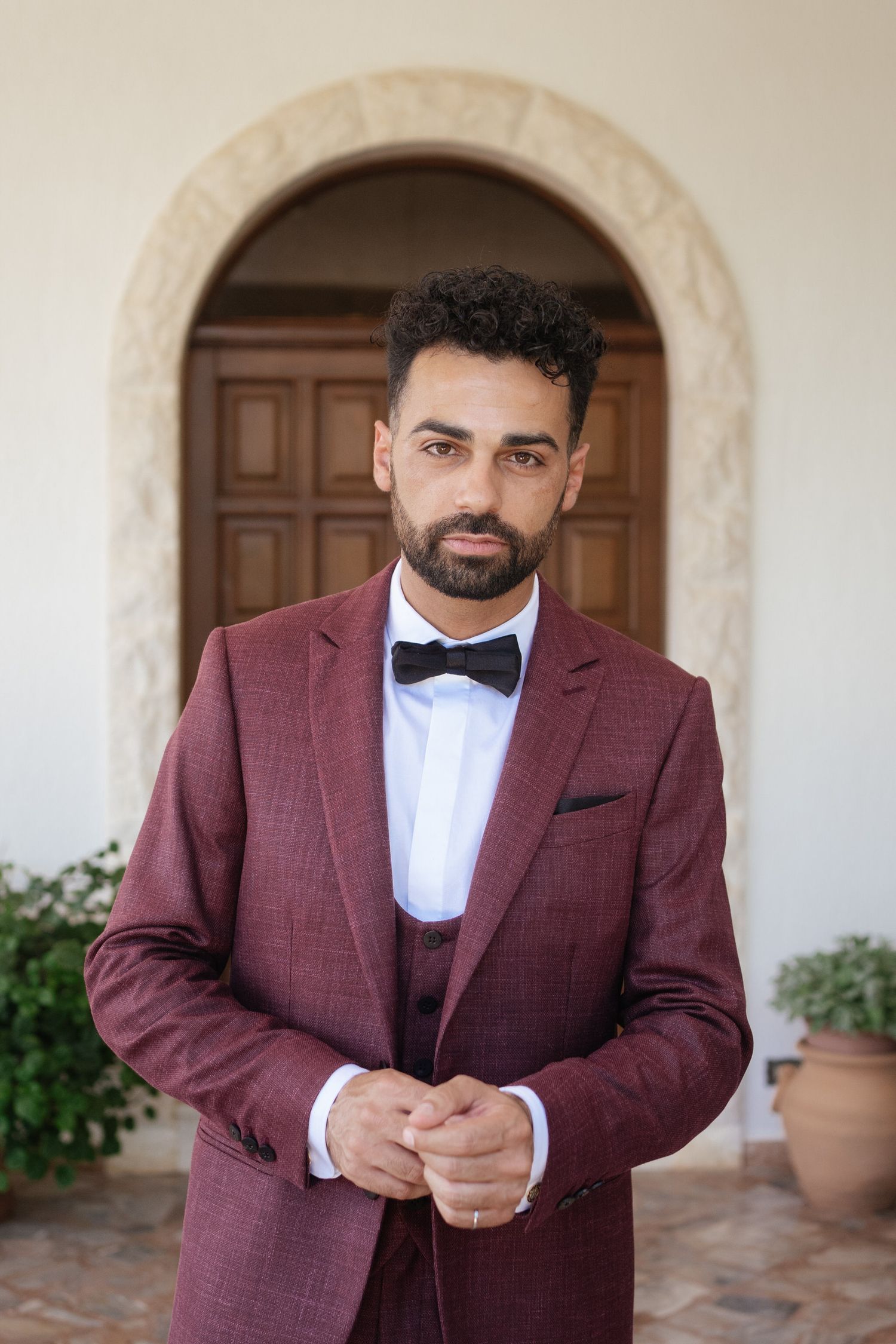 Multiple angles of someone in a burgundy suit adjusting their formal wear.