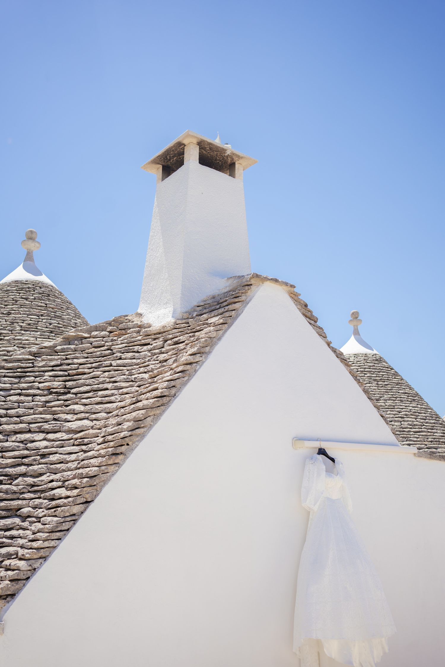 White stone trulli rooftops with distinctive cone shapes against bright blue sky.