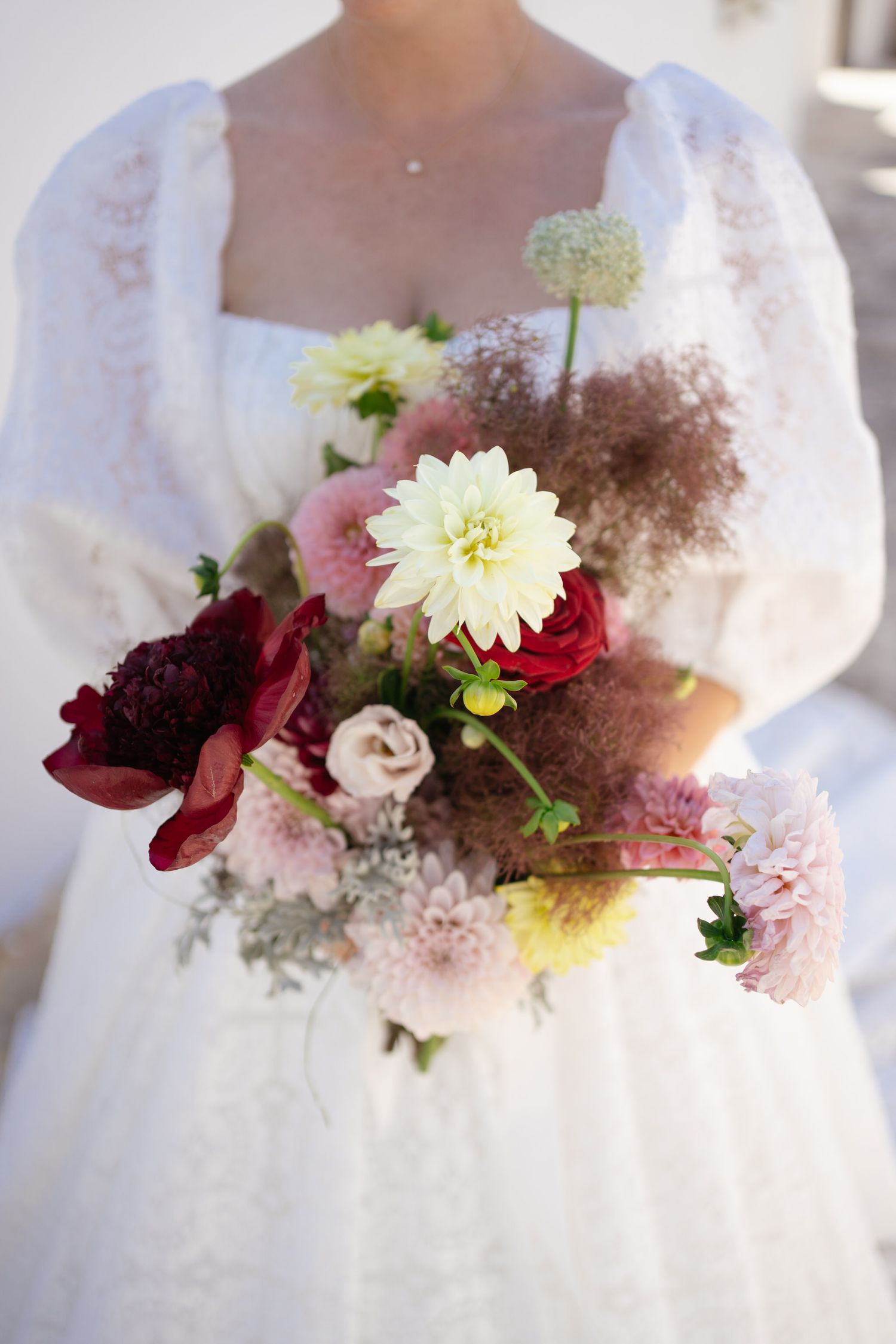 Beautiful wedding bouquet with red, white, and yellow flowers against lace white dress.