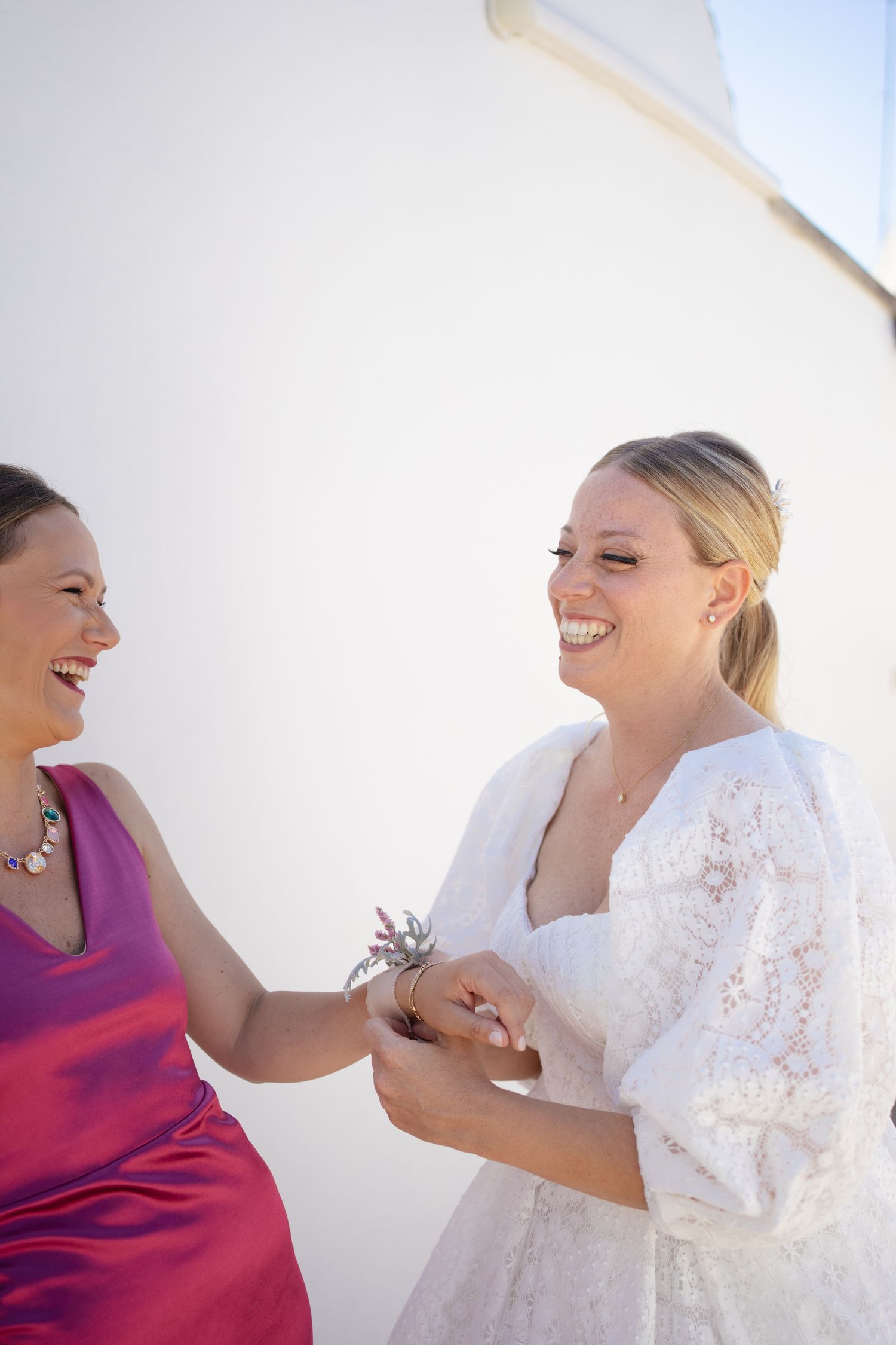 Joyful wedding moment captured against white stone wall background.