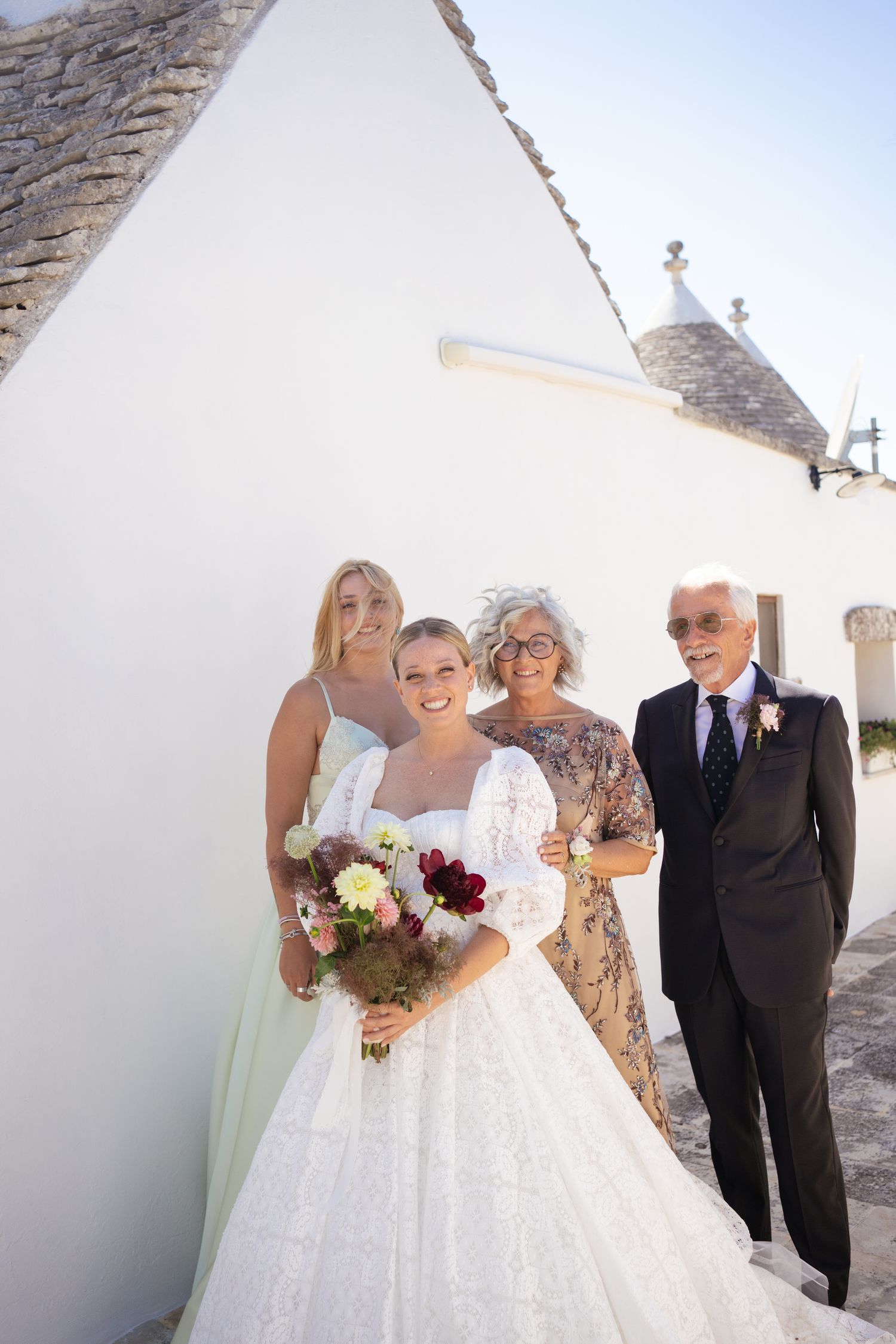 Wedding party gathered outside traditional trulli buildings for formal photos.