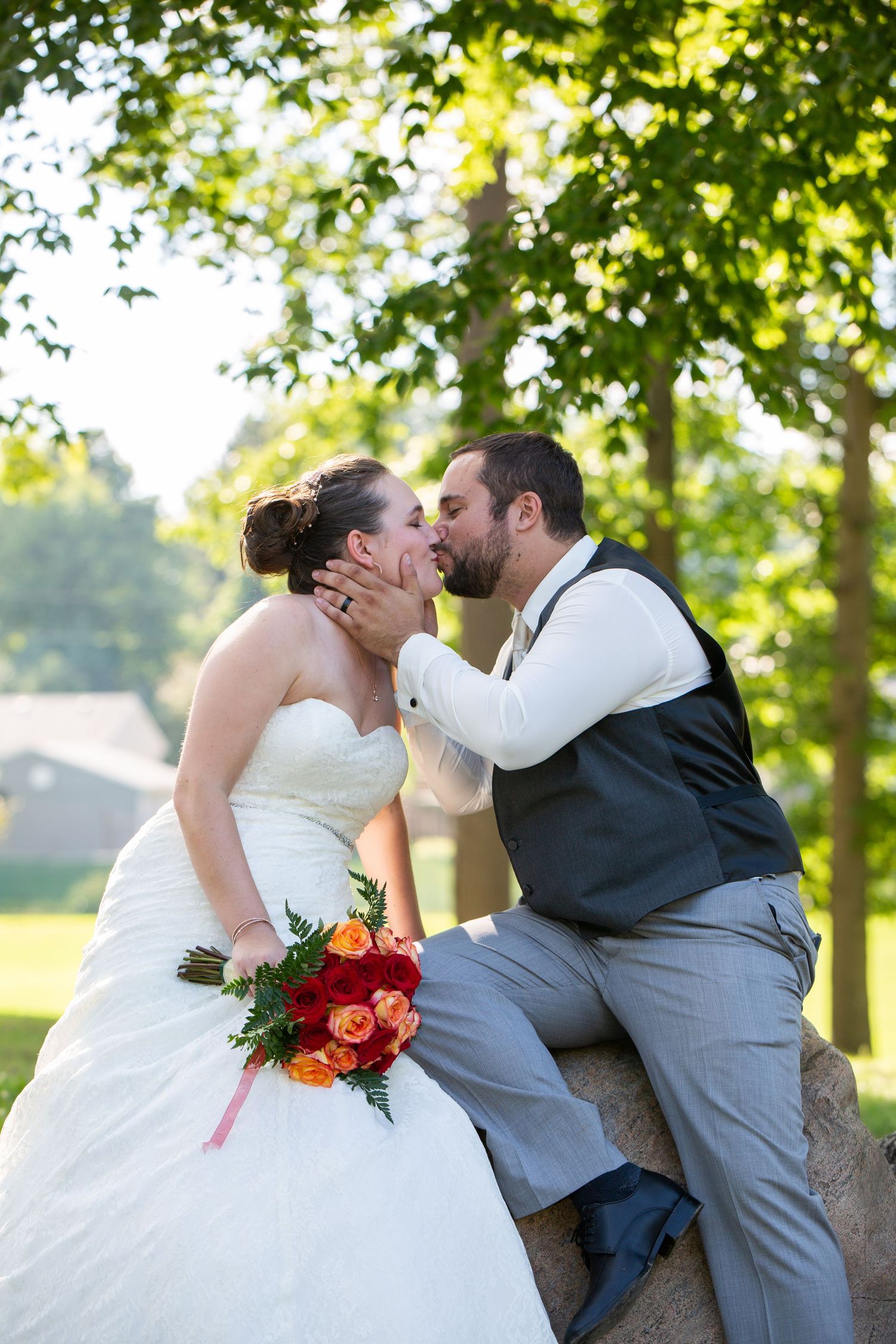 A romantic wedding kiss captured on a rock with orange flowers in the foreground.