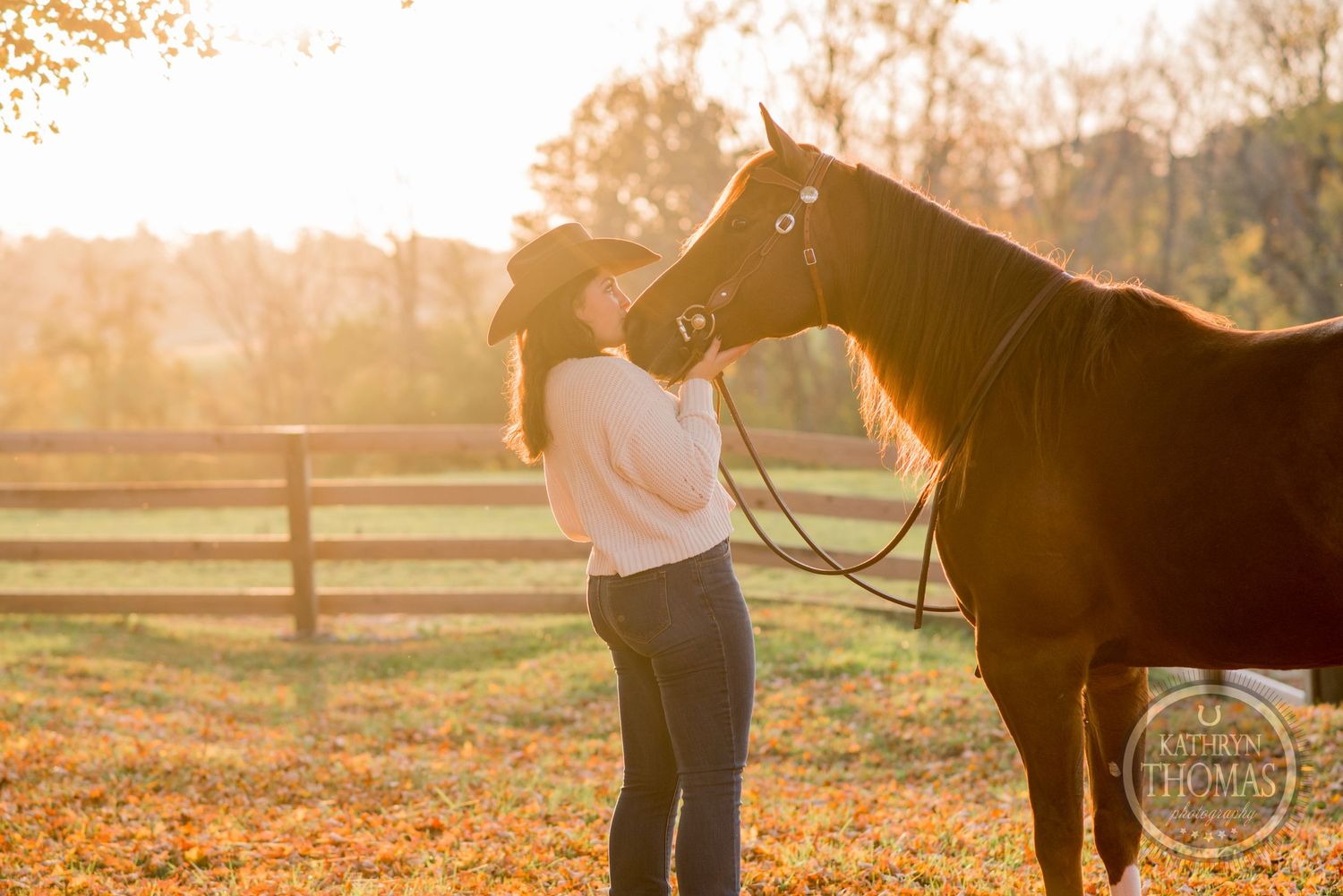 Golden sunset light illuminates a horse and rider sharing a tender moment by a wooden fence.