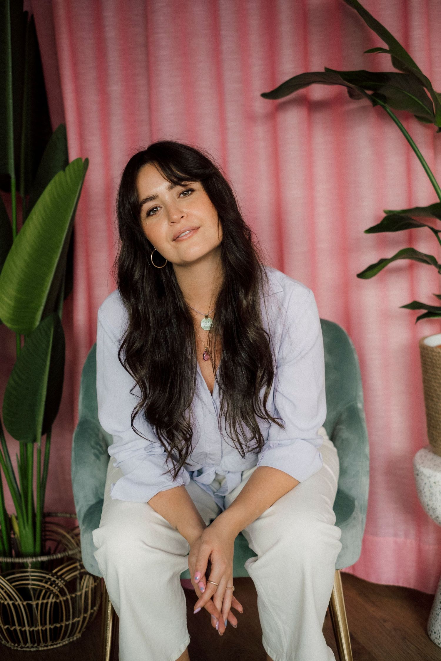 Portrait in front of pink curtain with tropical plants and bohemian decor.