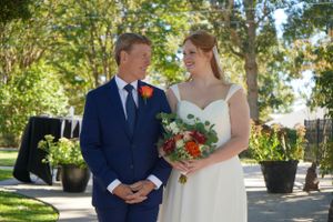 Bride and groom smiling together outdoors holding colorful floral bouquet.