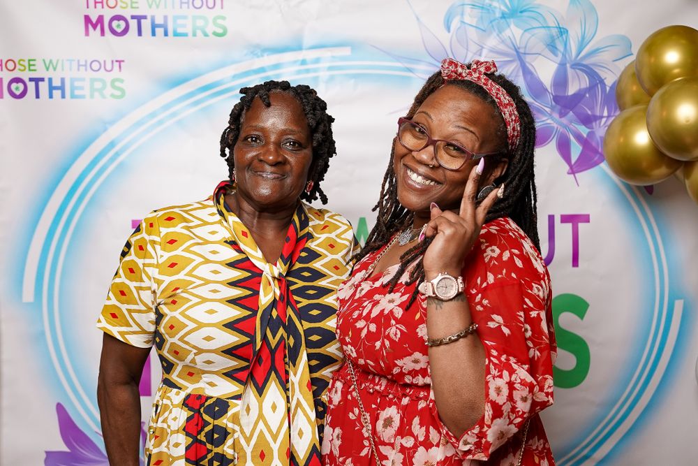 Event attendees posing against a branded backdrop with gold balloons and floral designs.