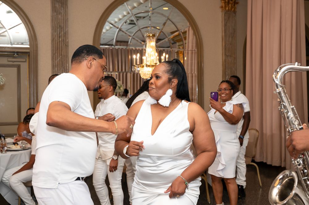 Group of people in white outfits dancing and celebrating at formal event.