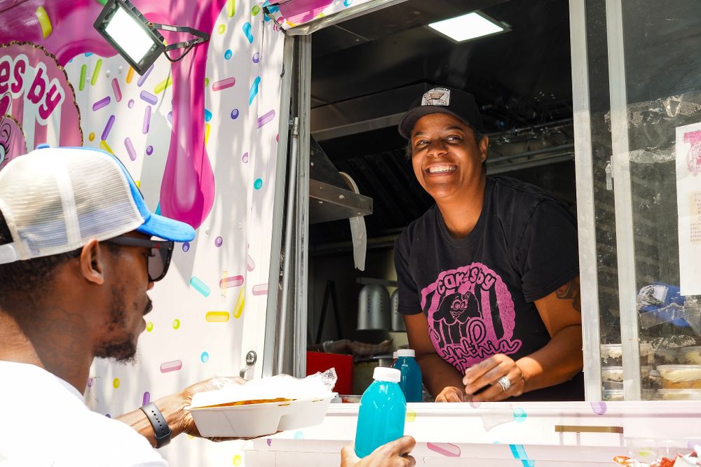 Food service workers smiling and serving from a mobile food truck window.