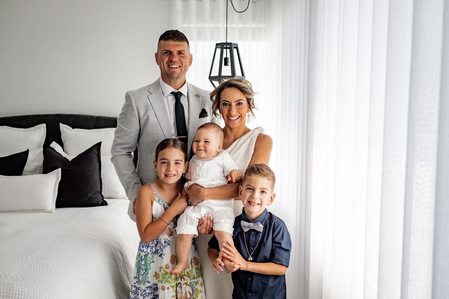 A loving family portrait captured in a contemporary white bedroom setting.