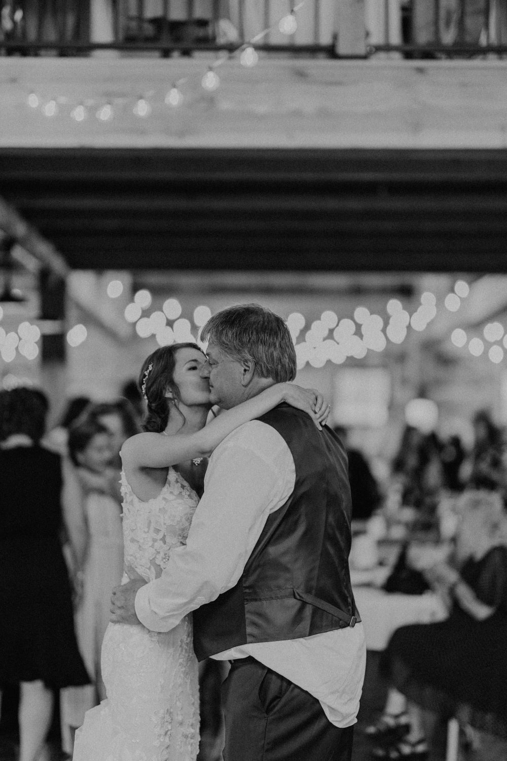 Black and white photo of bride kissing her father on the cheek during father-daughter wedding dance.