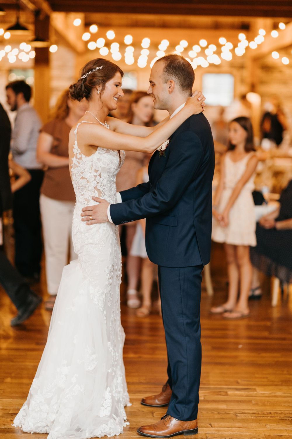 Bride and groom share their first dance, smiling at each other in a warmly lit barn wedding reception.