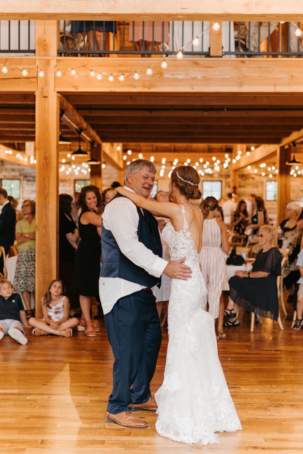Bride and her father laugh joyfully during their father-daughter dance at a rustic barn wedding reception.