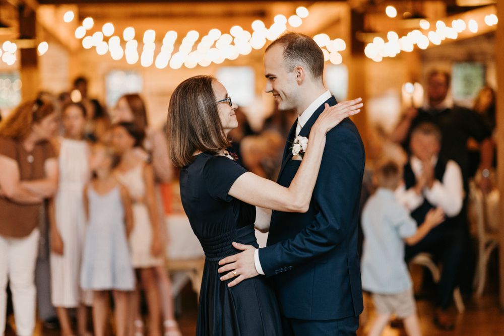 Couple sharing an intimate first dance at a wedding reception with string lights and guests in background.