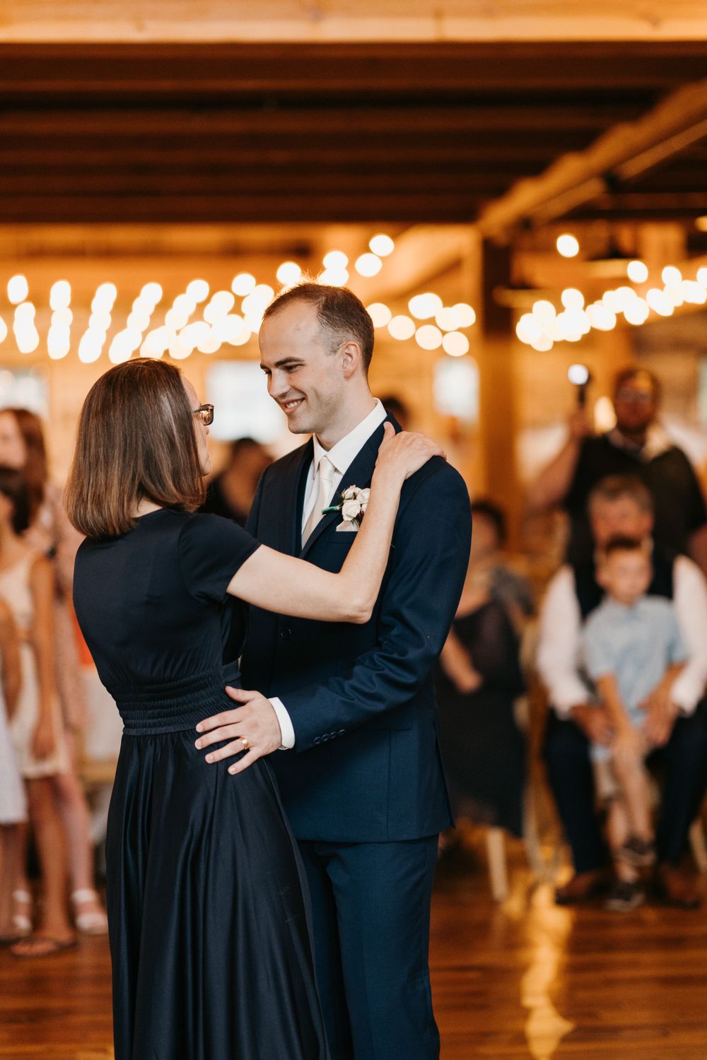 Smiling groom in navy suit dancing with woman in black dress at elegant wedding reception.