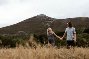 Maternity photographer Dublin. Stunning moment for pregnant couple as they await their new baby in golden field with mountain in background.