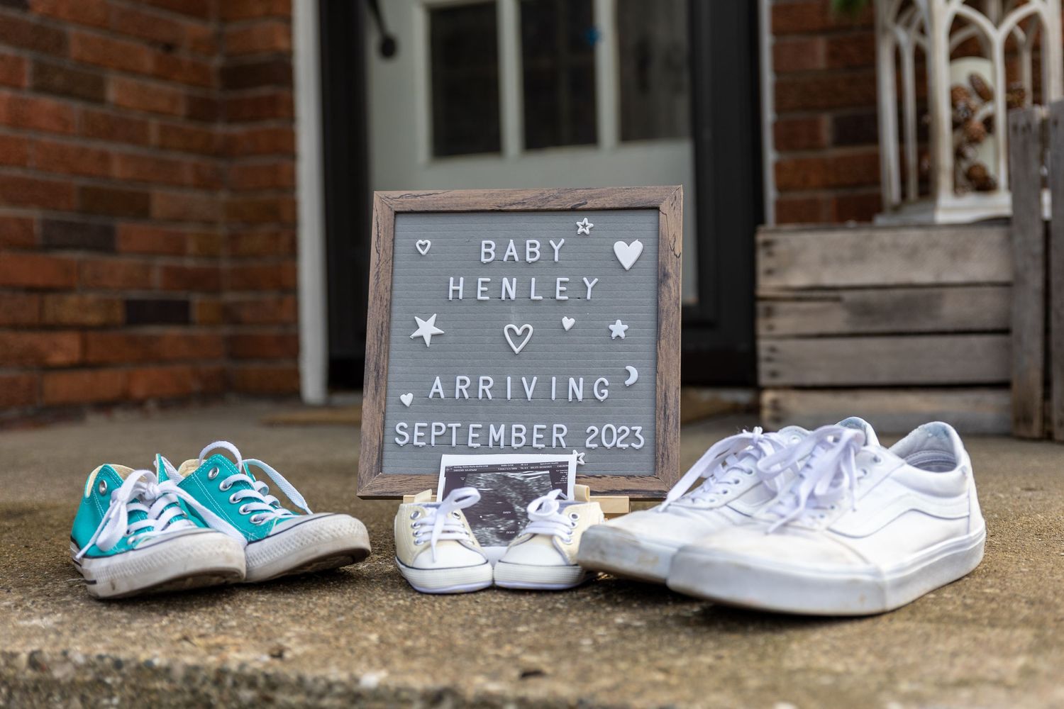 Baby announcement sign with sneakers and ultrasound photo reading Baby Henley Arriving September 2023.