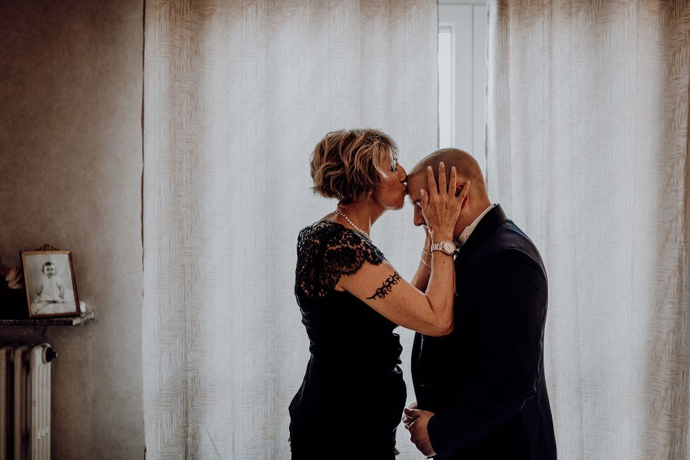 Tender moment as couple shares a kiss by window in elegant black attire.