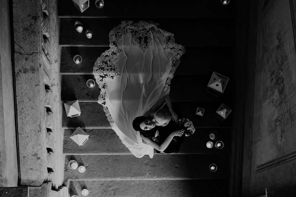 Aerial black and white photo of bride in flowing gown surrounded by candles on stone steps.