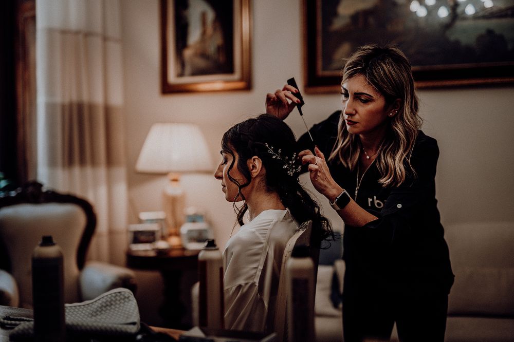 Hair stylist carefully styling bride's elegant updo in warmly lit room.