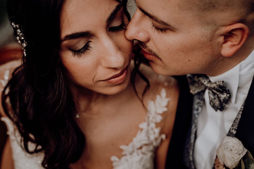 Close-up of bride and groom sharing intimate moment, bride in lace gown with floral hair accessories.