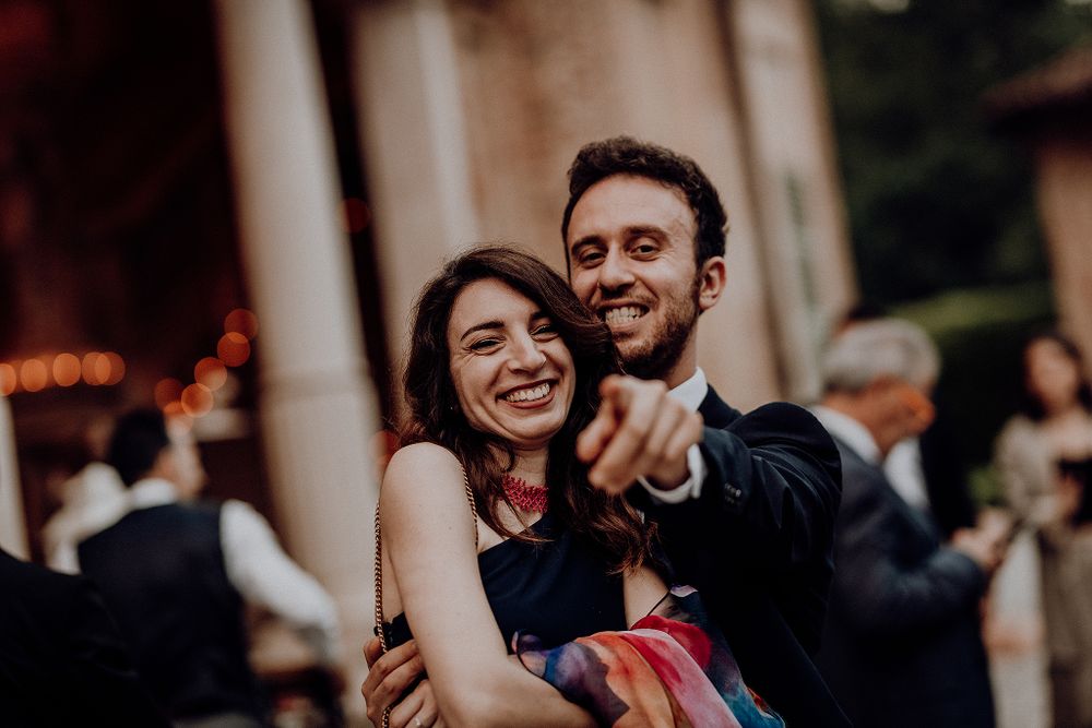 Joyful wedding guest couple laughing and dancing together outdoors at elegant evening reception.