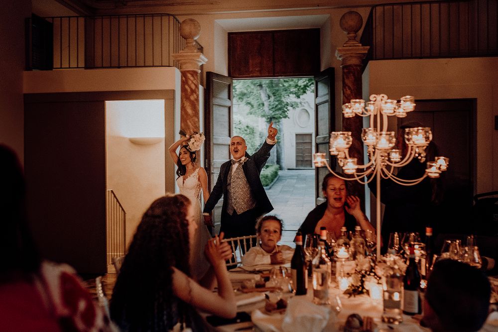 Bride and groom make grand entrance into candlelit wedding reception as guests celebrate at tables.