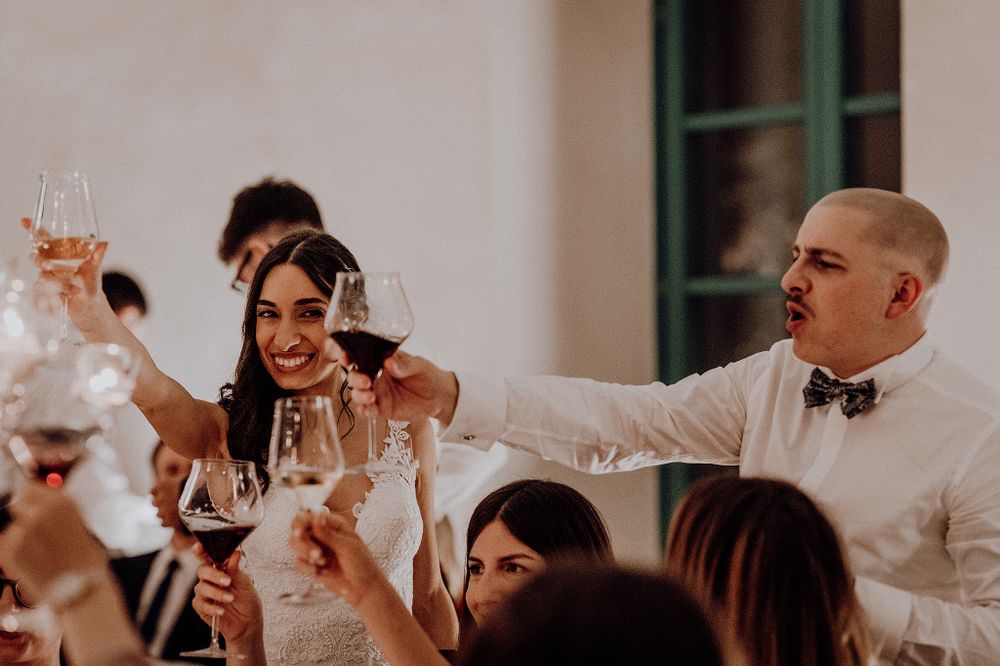 Bride and groom toasting with wine glasses surrounded by guests at wedding reception.