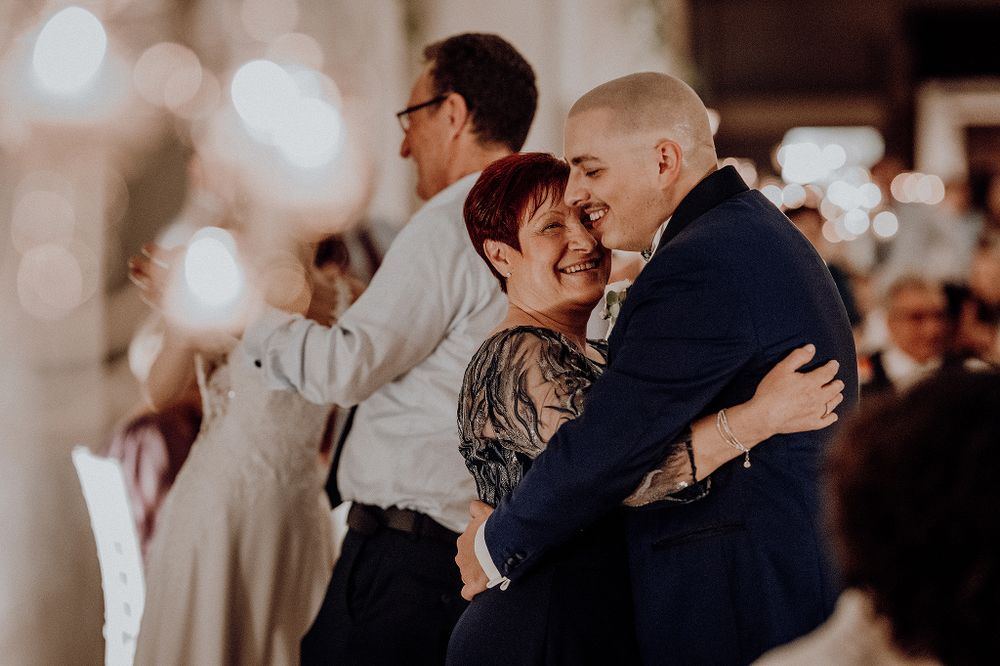 Groom embracing woman with floral tattoo during joyful wedding reception celebration.