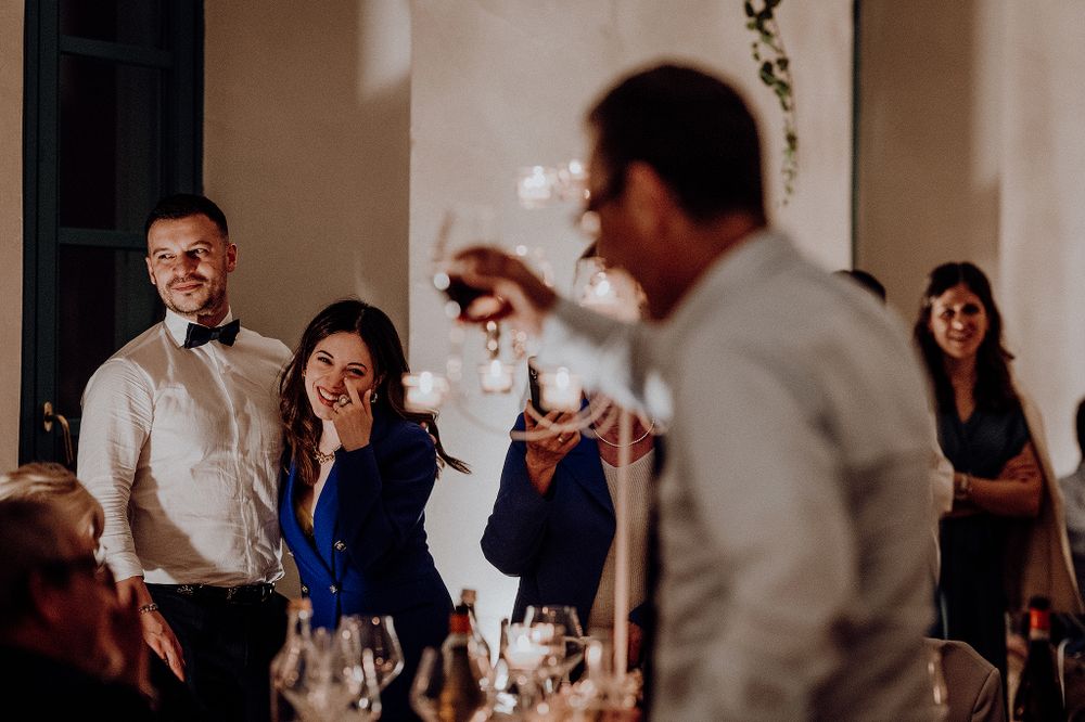 Wedding guests laughing and celebrating during reception toast in elegant venue.