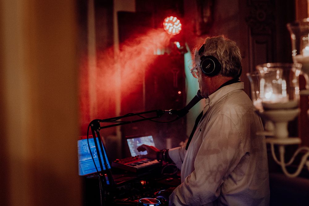 DJ wearing headphones operating mixing equipment under red stage lighting at a wedding reception.