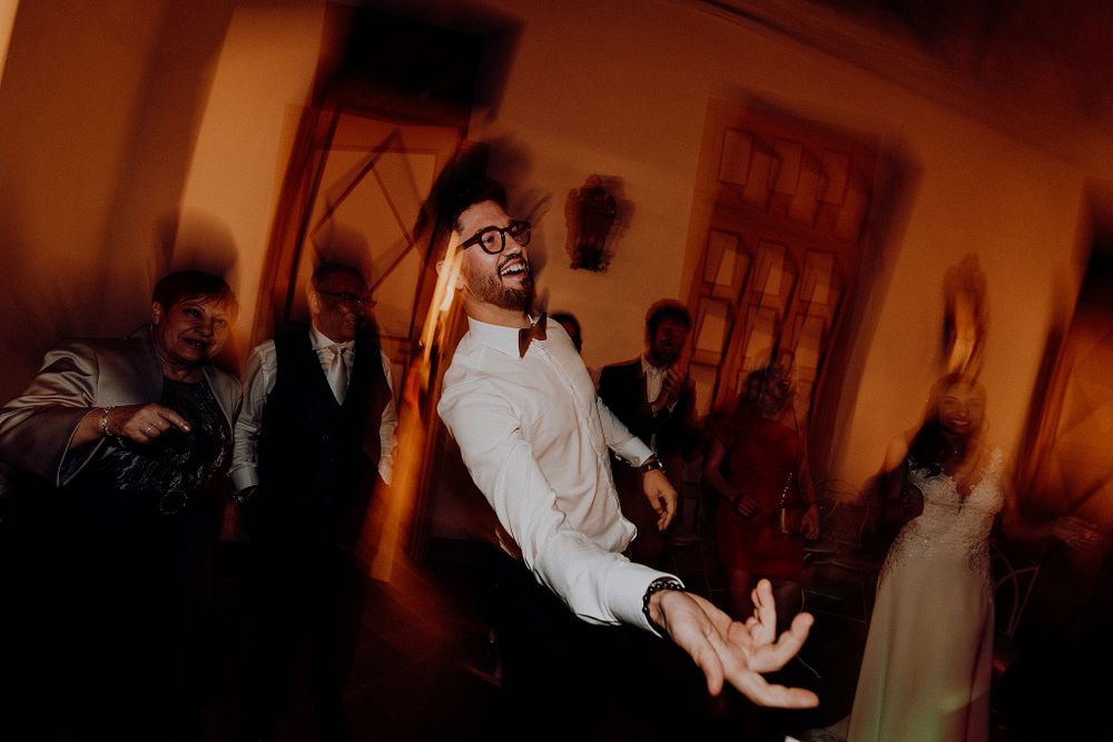 Energetic man in white shirt and glasses dancing enthusiastically at a wedding reception celebration.