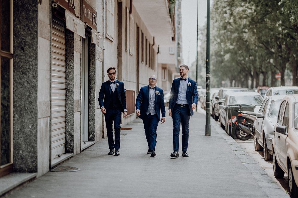 Three groomsmen in navy blue suits walking confidently down a city sidewalk on a wedding day.