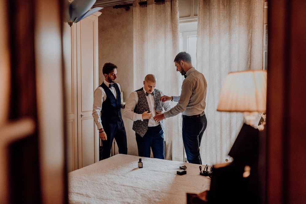 Groom and groomsmen helping each other get dressed in a hotel room before the wedding ceremony.