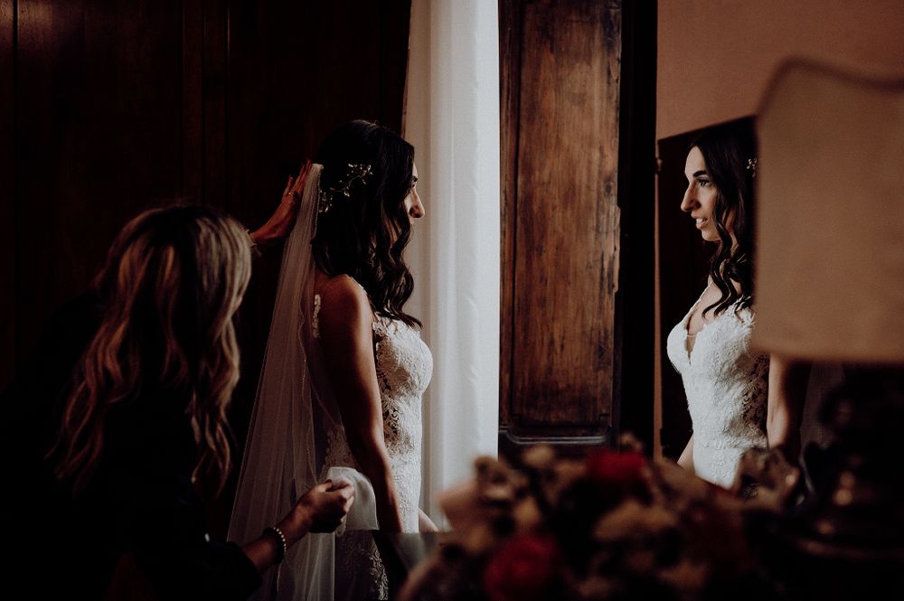 Bride in a lace wedding dress admiring her reflection in a mirror with bridesmaid.